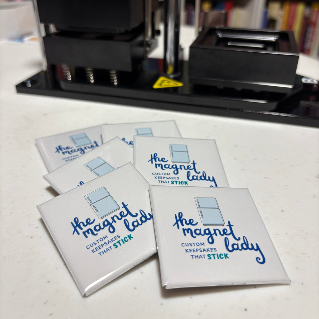 Set of magnets with 'The Magnet Lady' branding on a surface with a magnet press and bookshelf in the background.