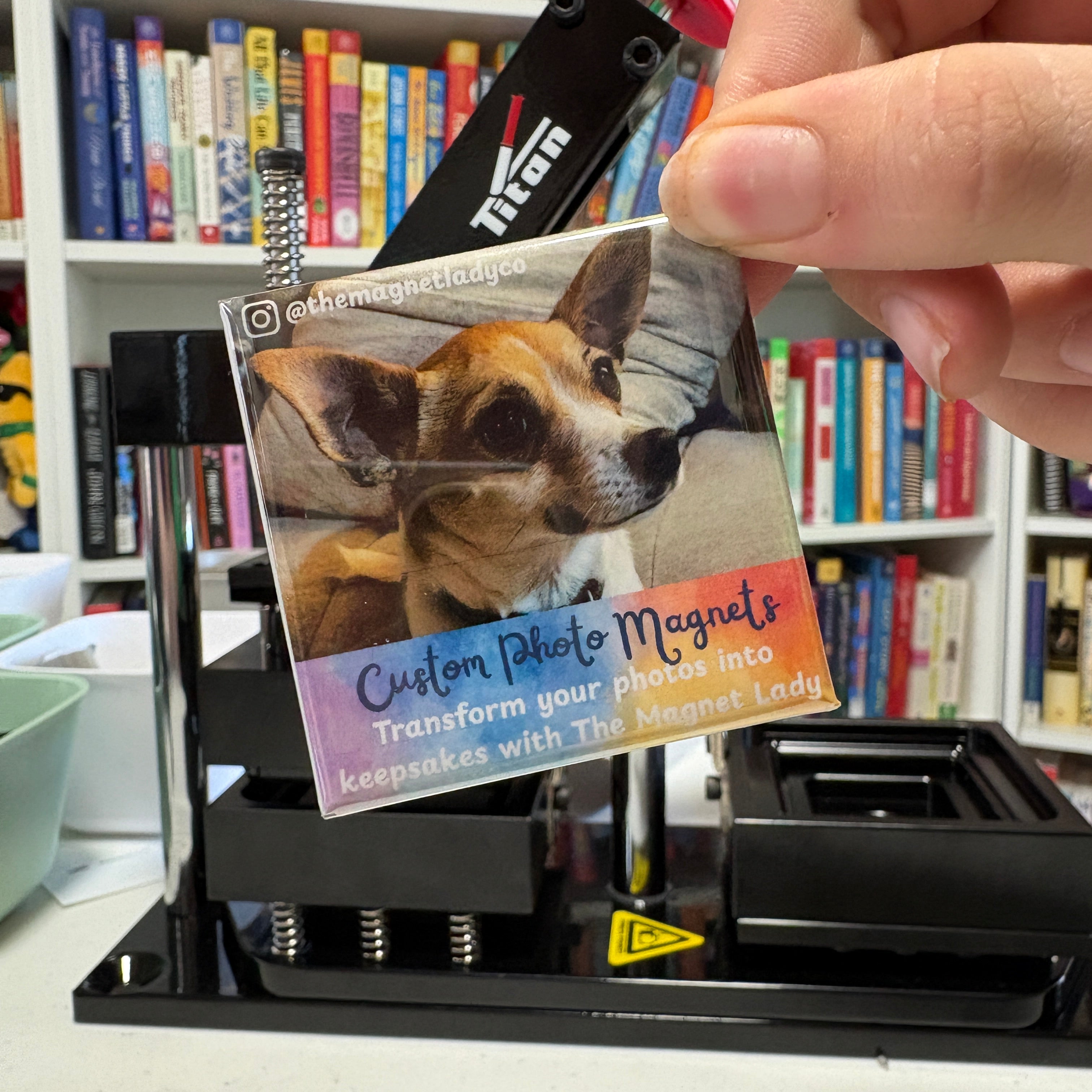 Hand showing a photo magnet with a magnet press and books in the background