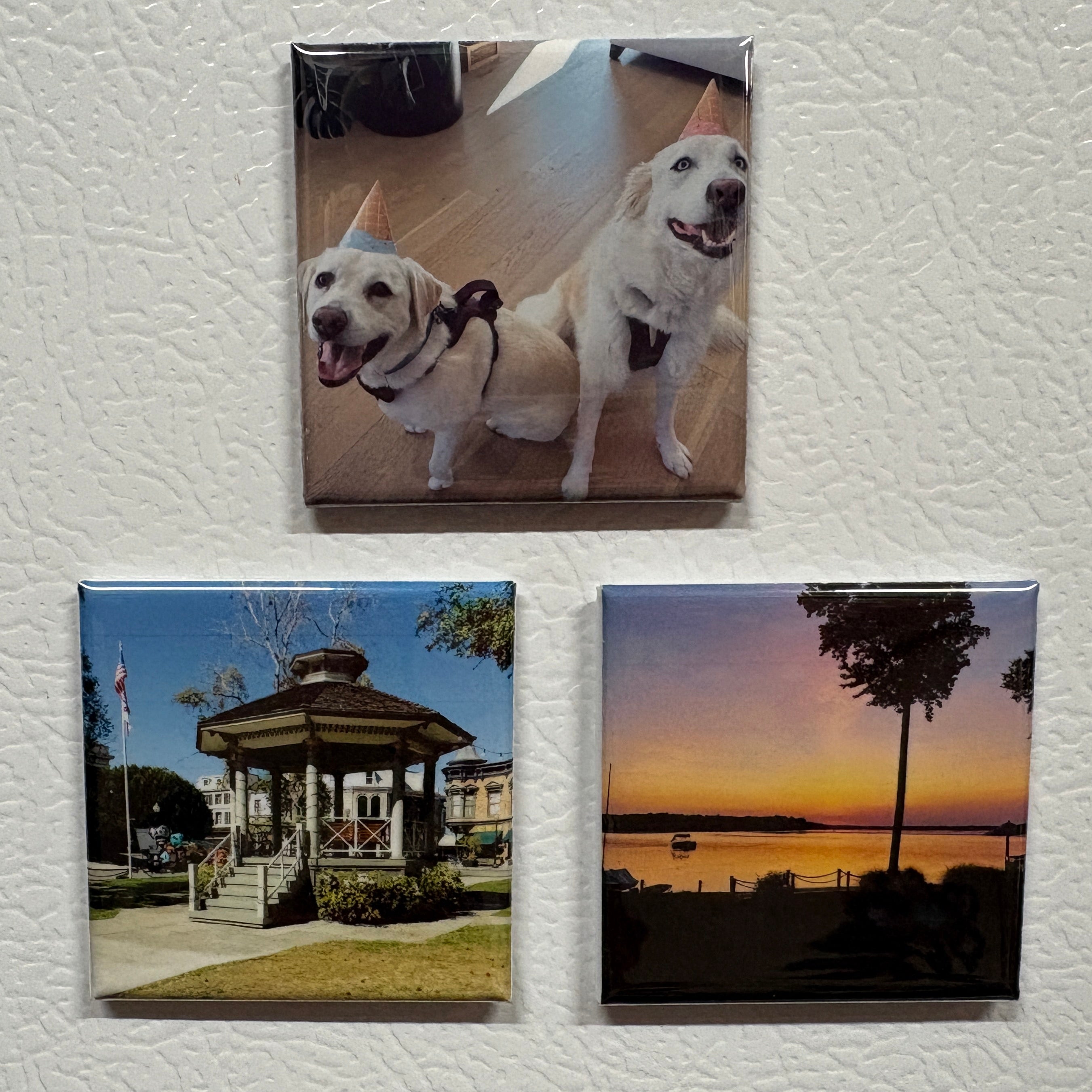 Three square magnets on a textured white surface, featuring images of dogs, a gazebo, and a sunset.